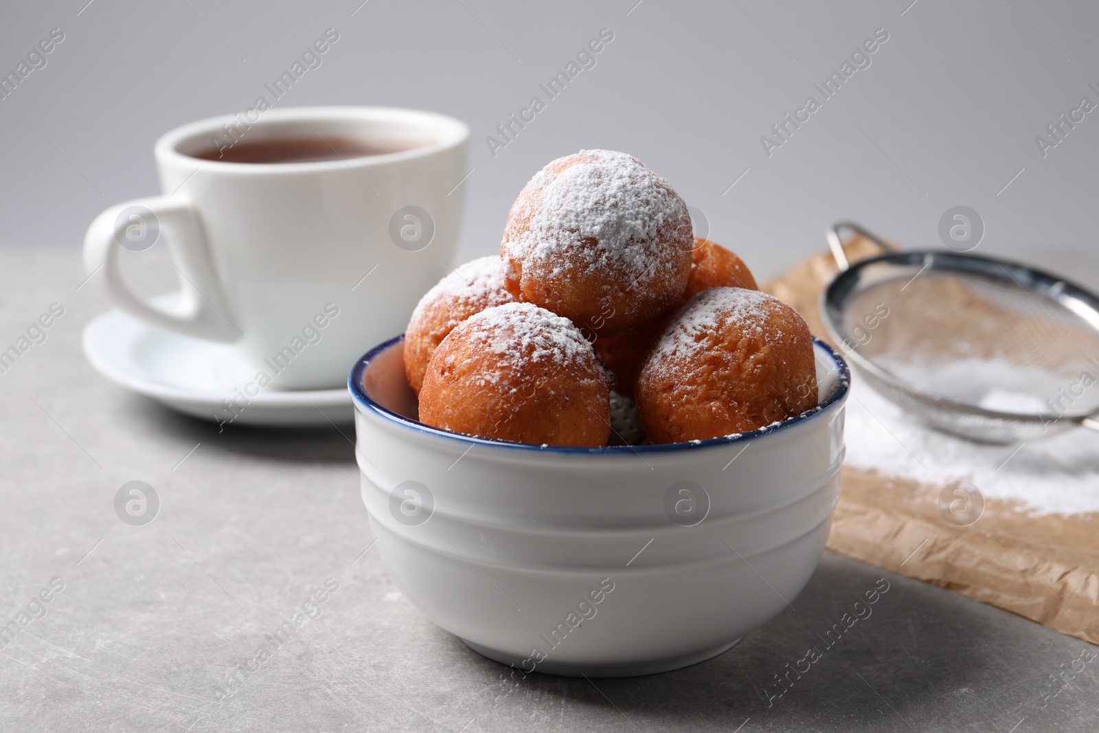 Photo of Delicious sweet buns in bowl, cup of drink and strainer on gray table