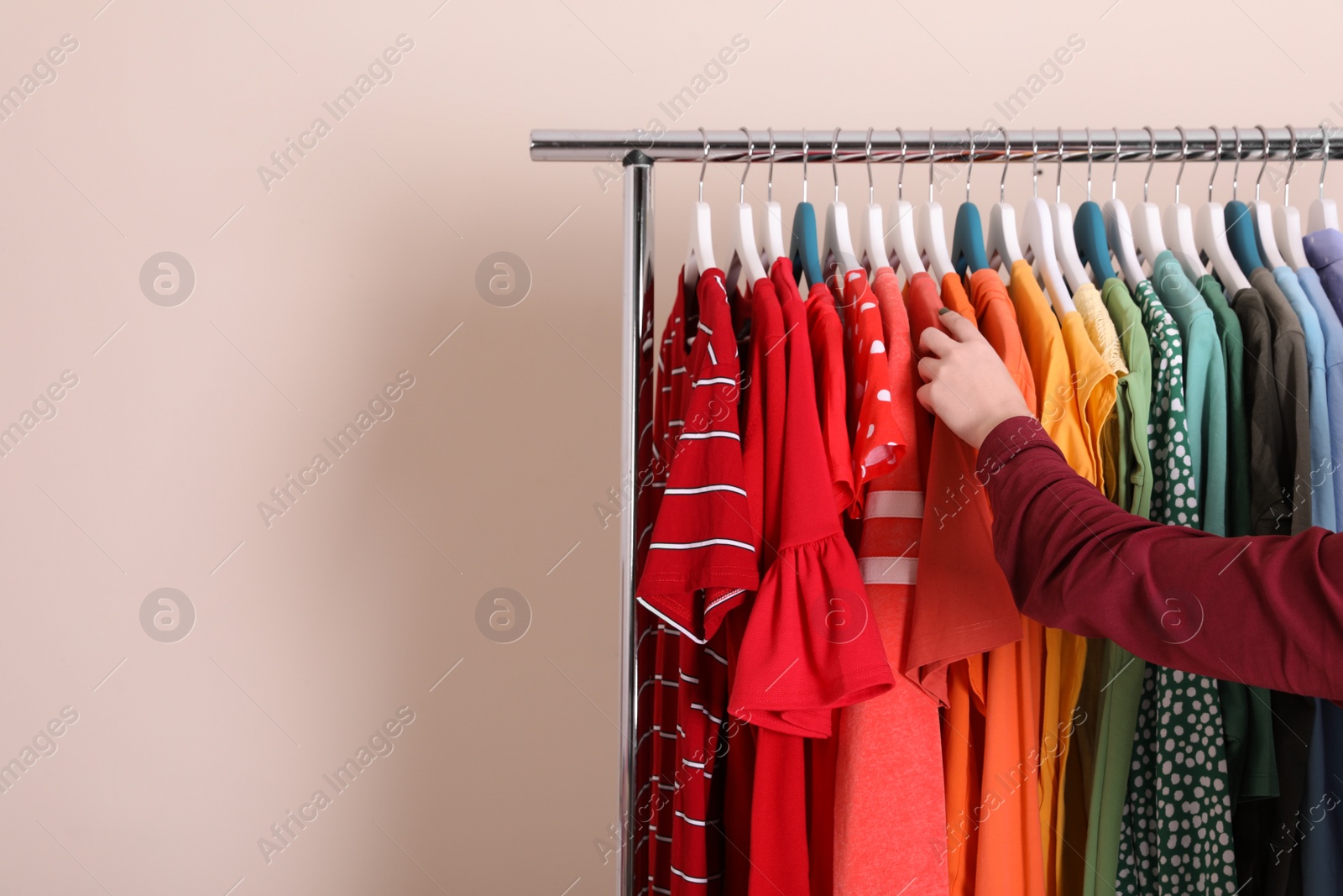 Photo of Woman choosing clothes from wardrobe rack on color background. Space for text