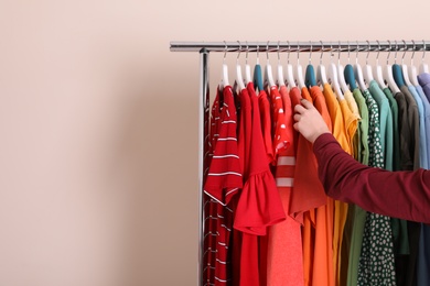 Photo of Woman choosing clothes from wardrobe rack on color background. Space for text