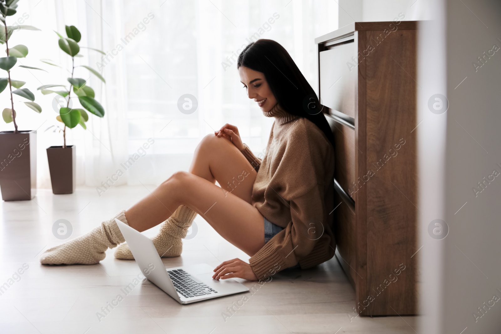 Photo of Woman with laptop sitting on warm floor at home. Heating system