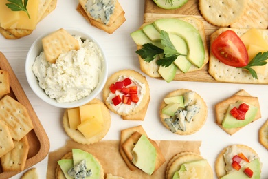 Photo of Different snacks with salted crackers on white wooden table, flat lay