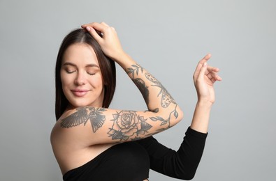 Beautiful woman with tattoos on arm against grey background