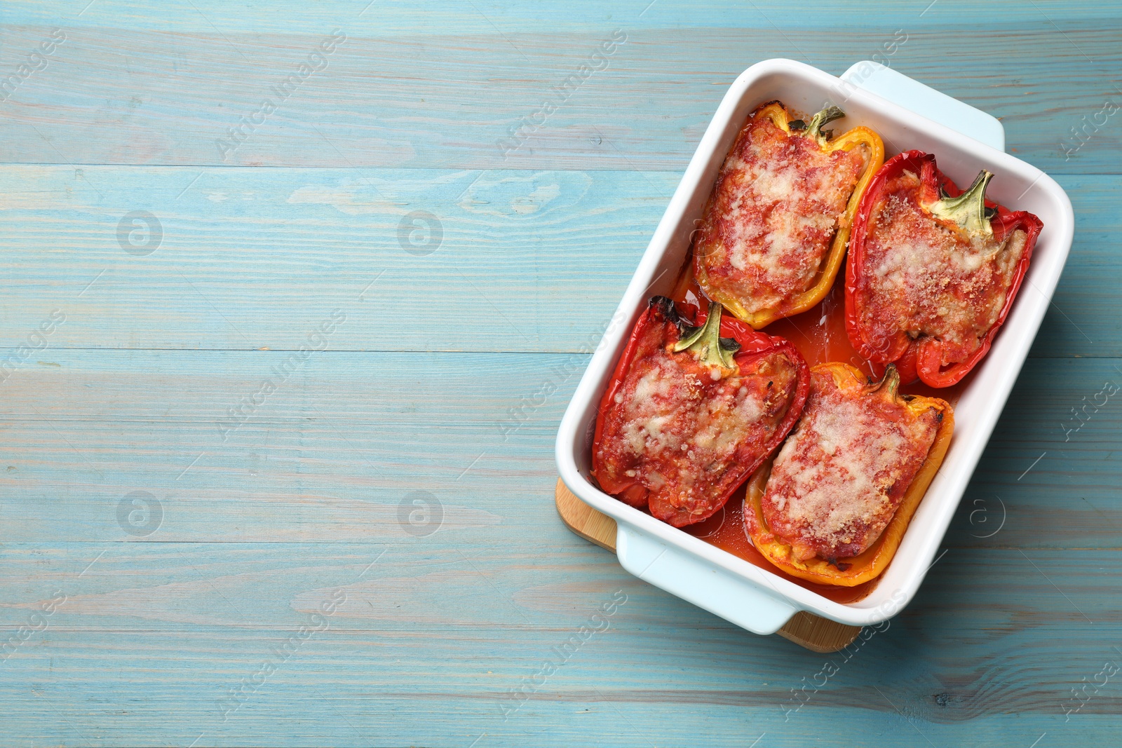 Photo of Tasty stuffed peppers in dish on light blue wooden table, top view. Space for text