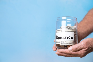 Man holding jar with money and label DONATION on color background, closeup. Space for text