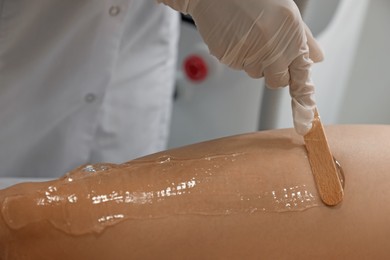 Professional cosmetologist applying gel on client's leg before laser epilation procedure in salon, closeup