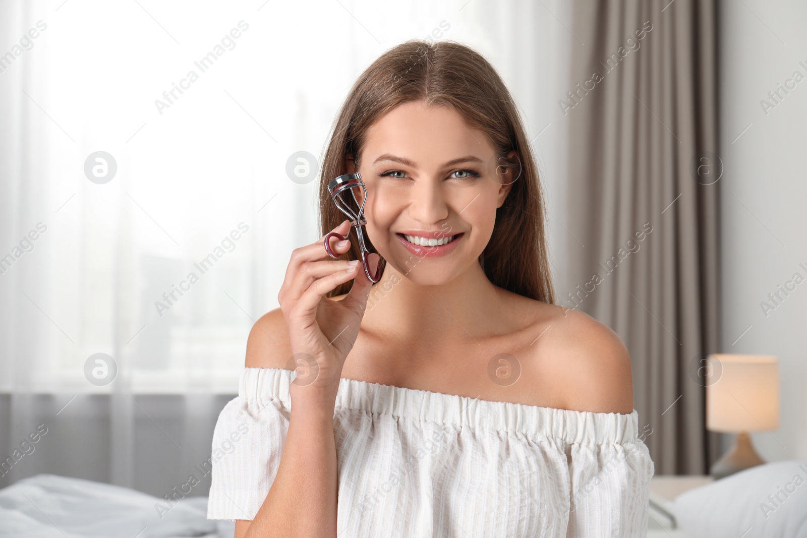 Photo of Young woman holding eyelash curler at home