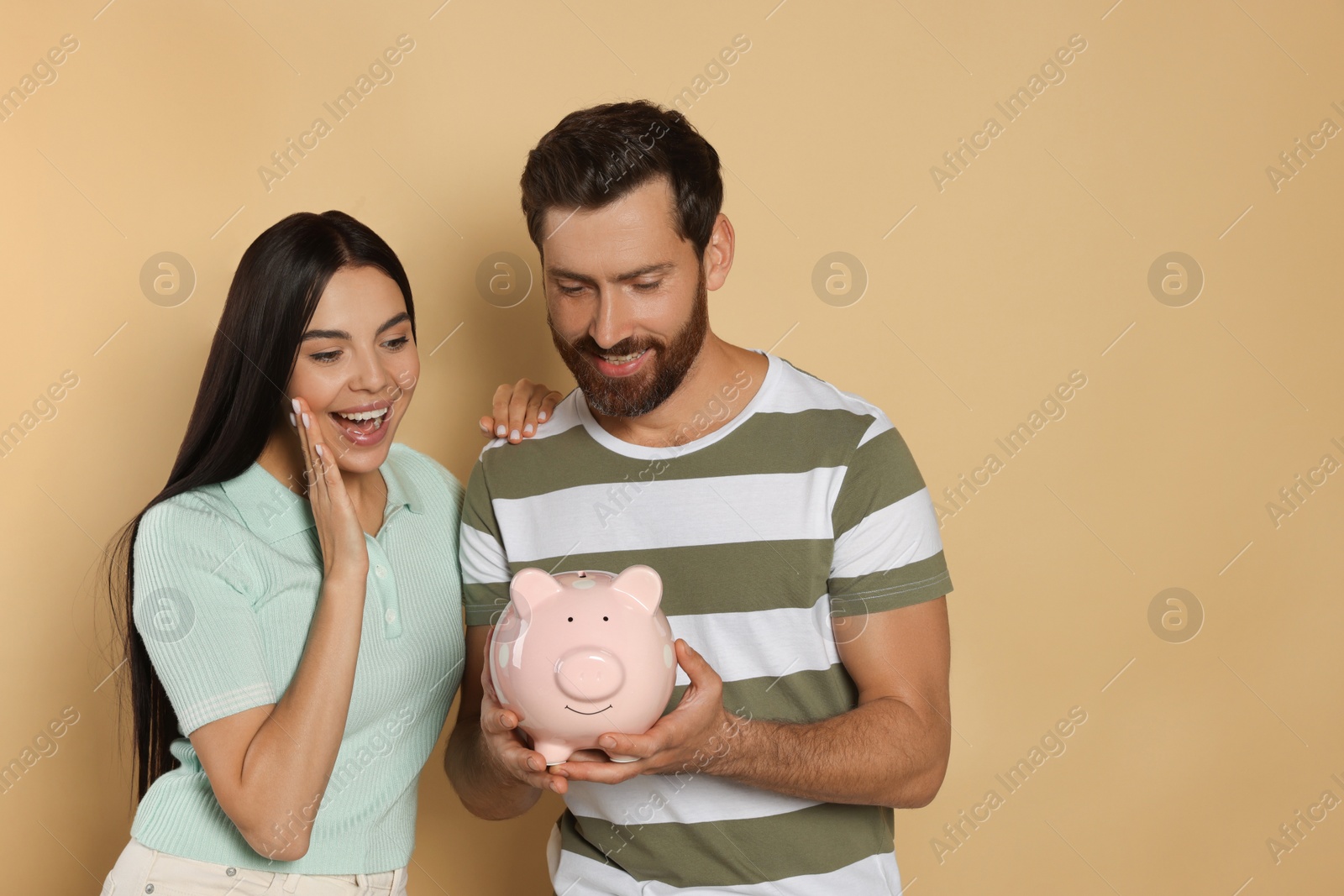 Photo of Happy couple with ceramic piggy bank on beige background