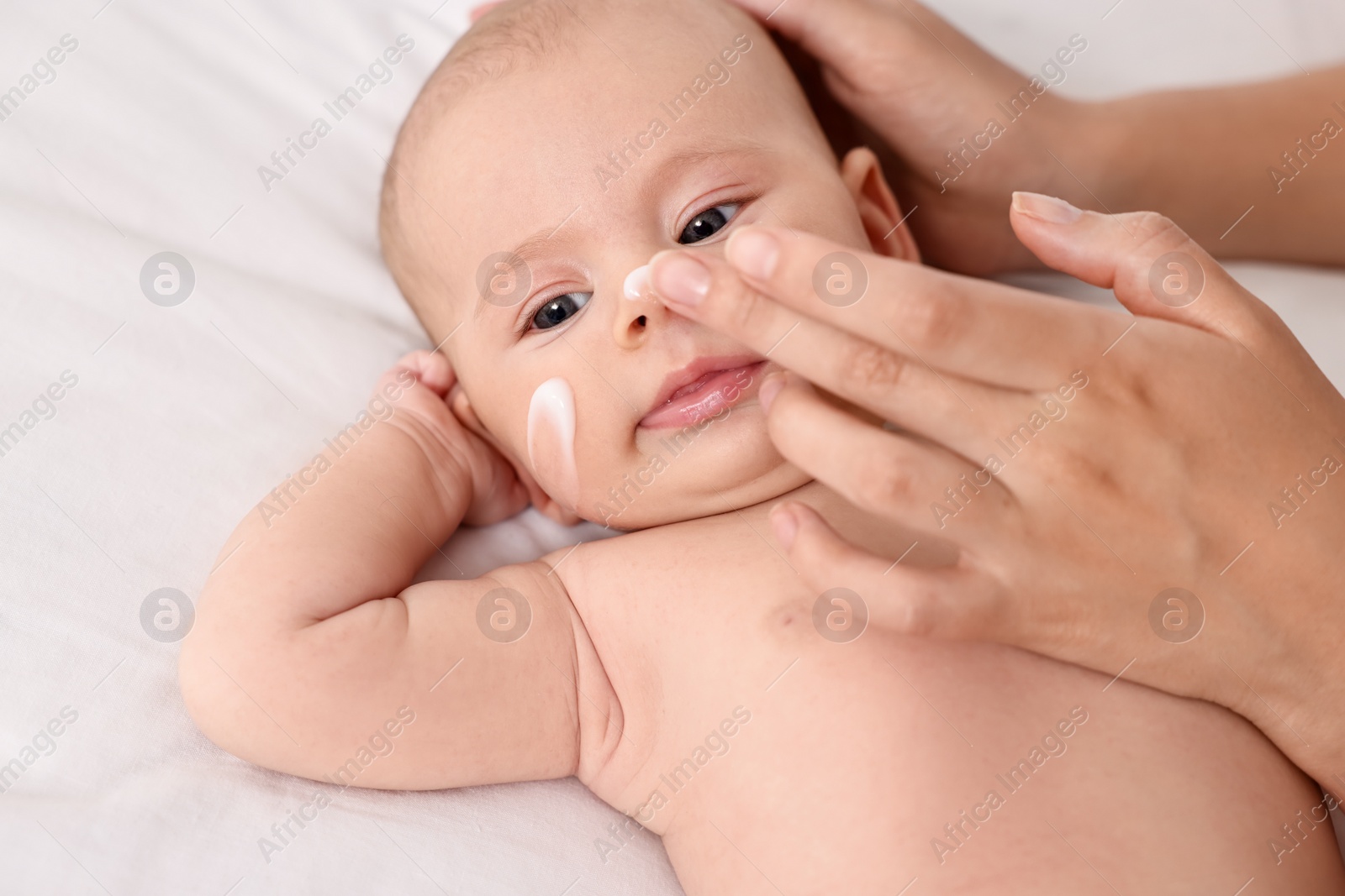 Photo of Woman applying cream onto baby`s face on bed, closeup