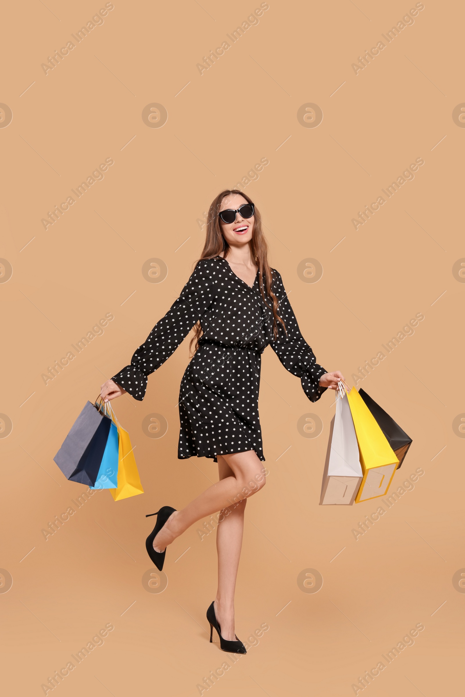 Photo of Stylish young woman in sunglasses with shopping bags on beige background