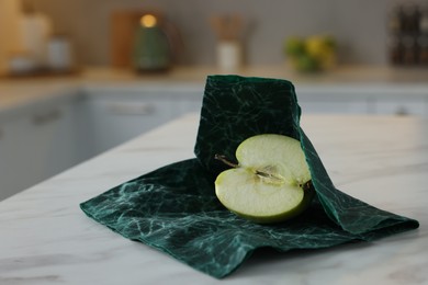 Photo of Half of apple with green beeswax food wrap on white table