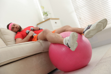 Photo of Lazy young man with sport equipment on sofa at home, focus on legs