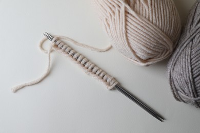 Soft colorful yarns and metal knitting needles on light background, top view