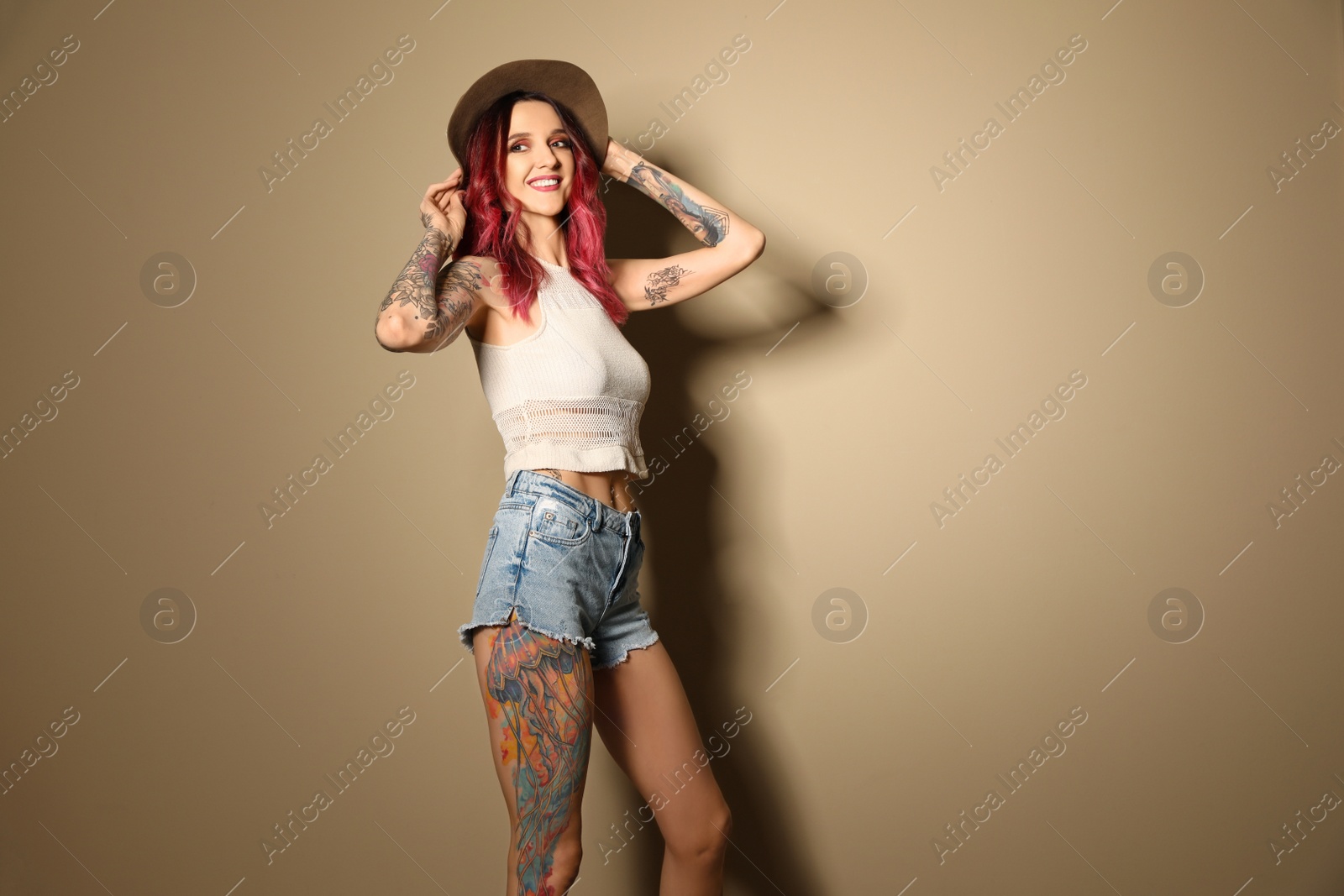 Photo of Beautiful woman with tattoos on body against beige background