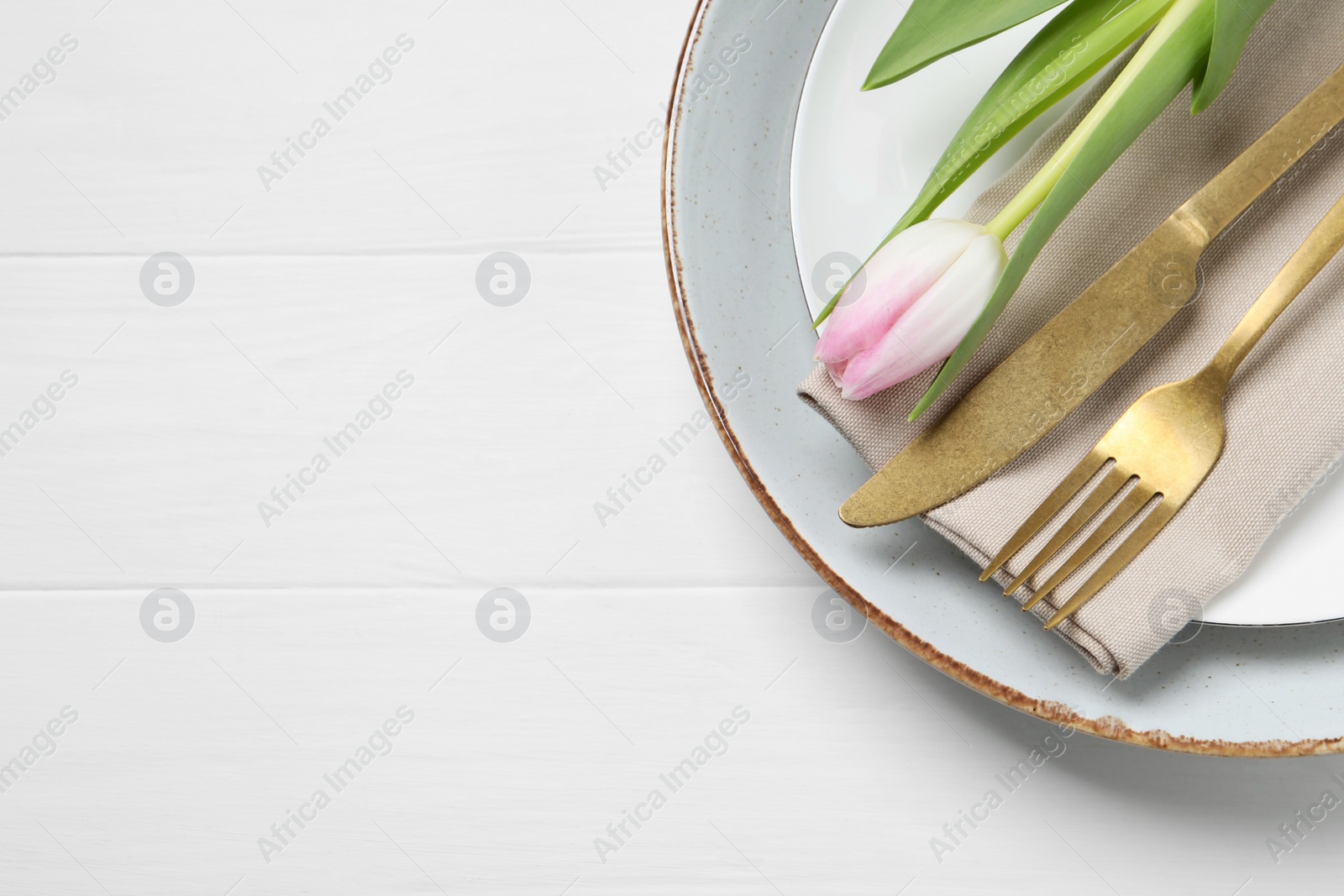 Photo of Stylish table setting with cutlery and tulip on white wooden background, top view. Space for text