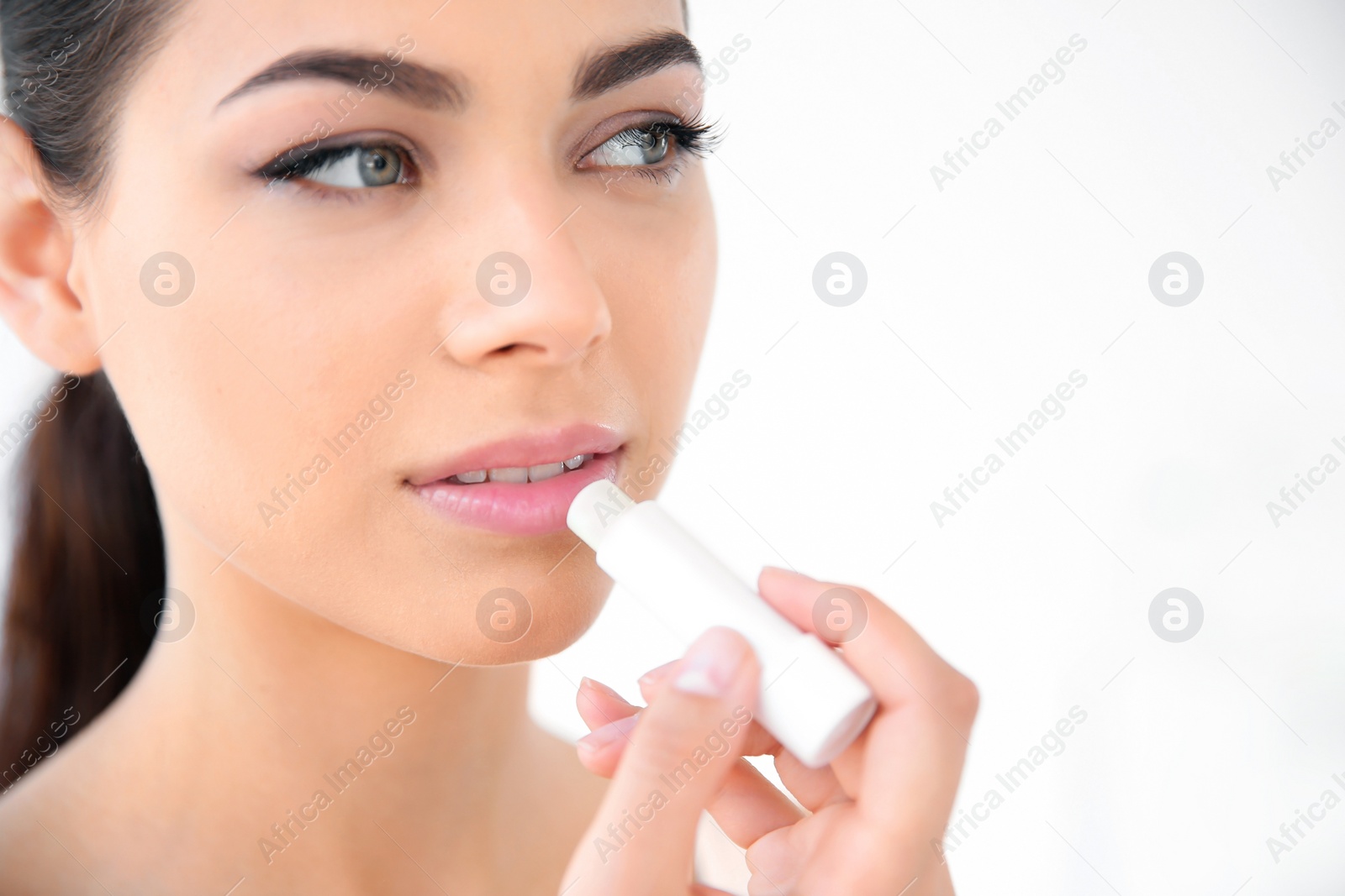 Photo of Young woman applying balm on her lips against light background