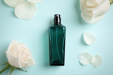 Photo of Bottle of perfume, beautiful roses and petals on light blue background, flat lay