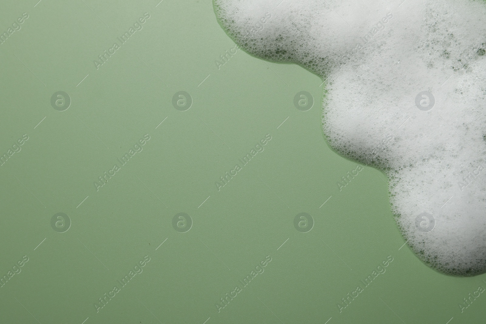 Photo of Fluffy soap foam on green background, above view. Space for text