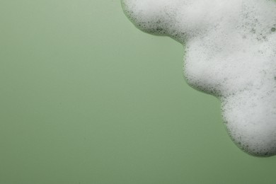 Photo of Fluffy soap foam on green background, above view. Space for text