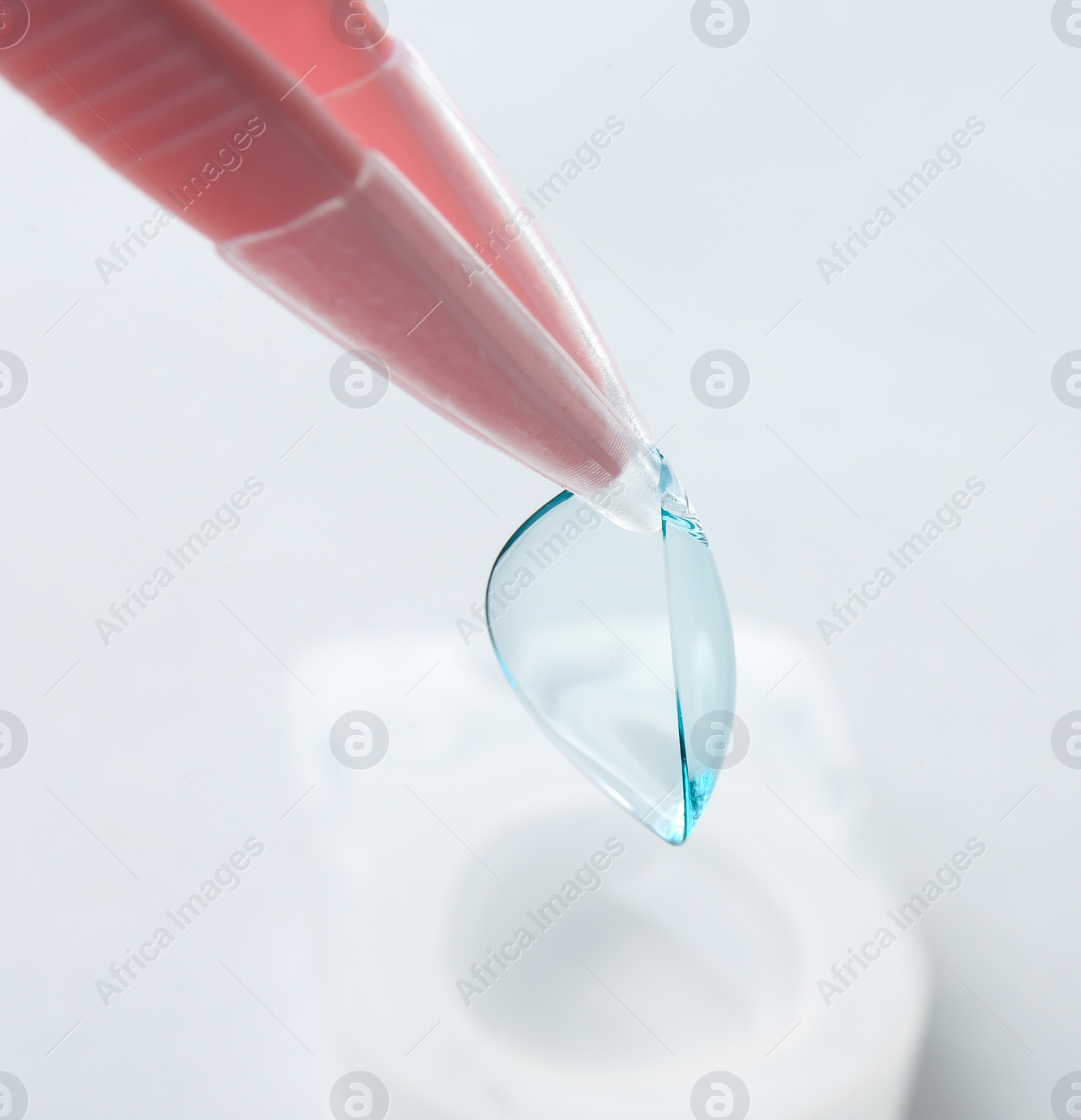 Photo of Tweezers with contact lens on light background, closeup