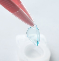 Tweezers with contact lens on light background, closeup