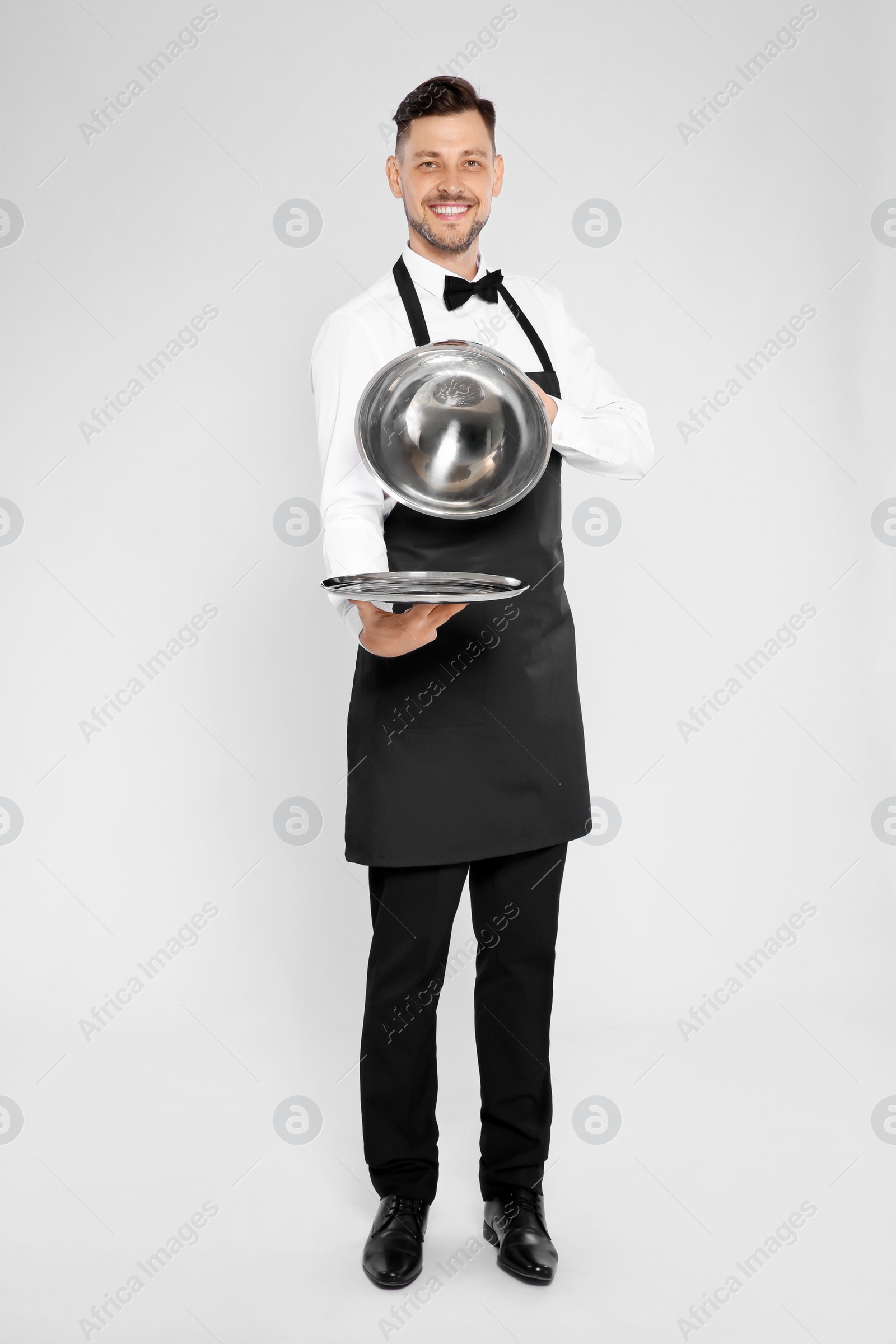 Photo of Handsome waiter holding metal tray with lid on light background