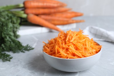 Photo of Grated carrot in bowl on light grey marble table, closeup