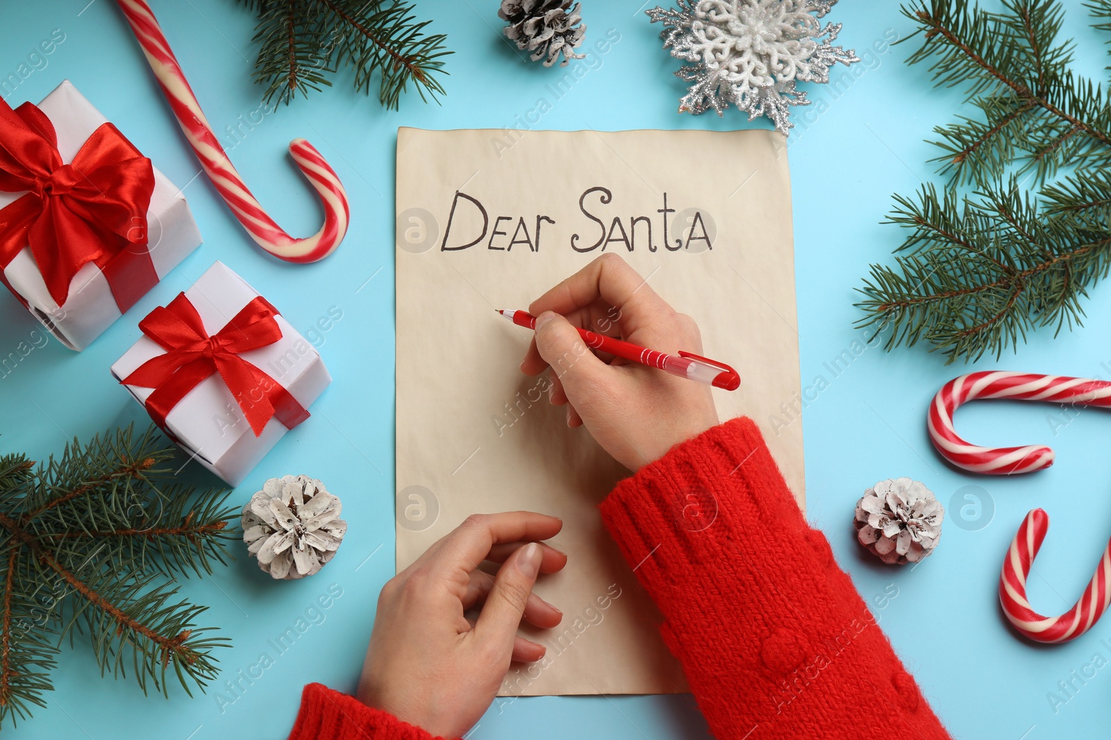 Photo of Top view of woman writing letter to Santa at light blue table, closeup