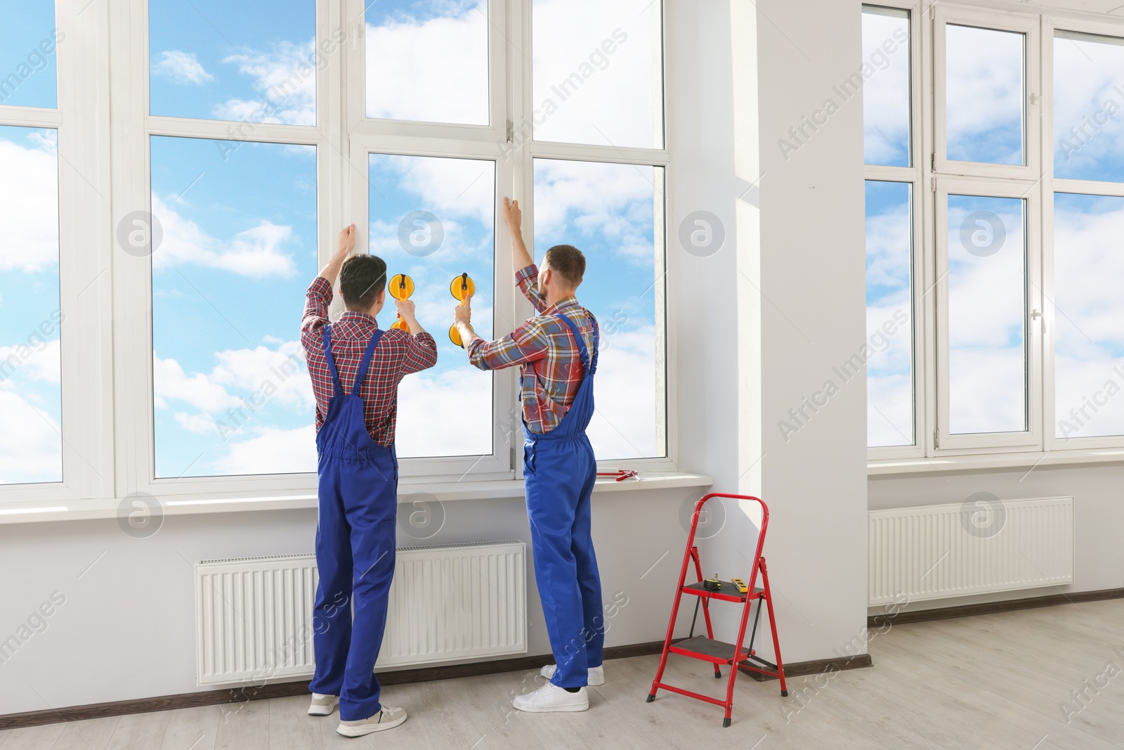 Photo of Workers using suction lifters during plastic window installation indoors