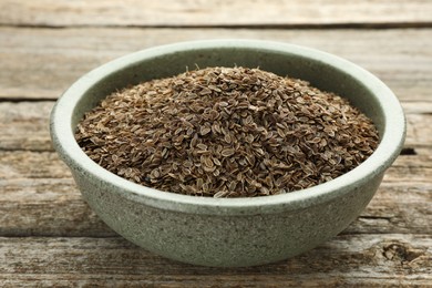 Dry dill seeds in bowl on wooden table, closeup