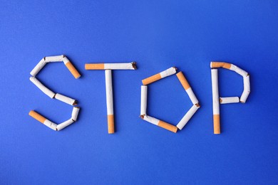 Photo of Word Stop made of cigarettes on blue background, flat lay. Quitting smoking concept