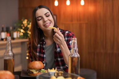 Photo of Young woman eating french fries and tasty burger in cafe. Space for text