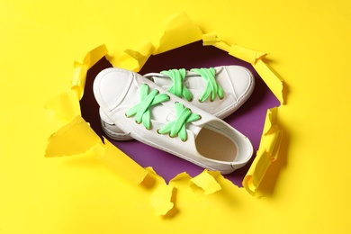 Stylish sneakers with shoe laces on purple background, view through hole in torn yellow paper