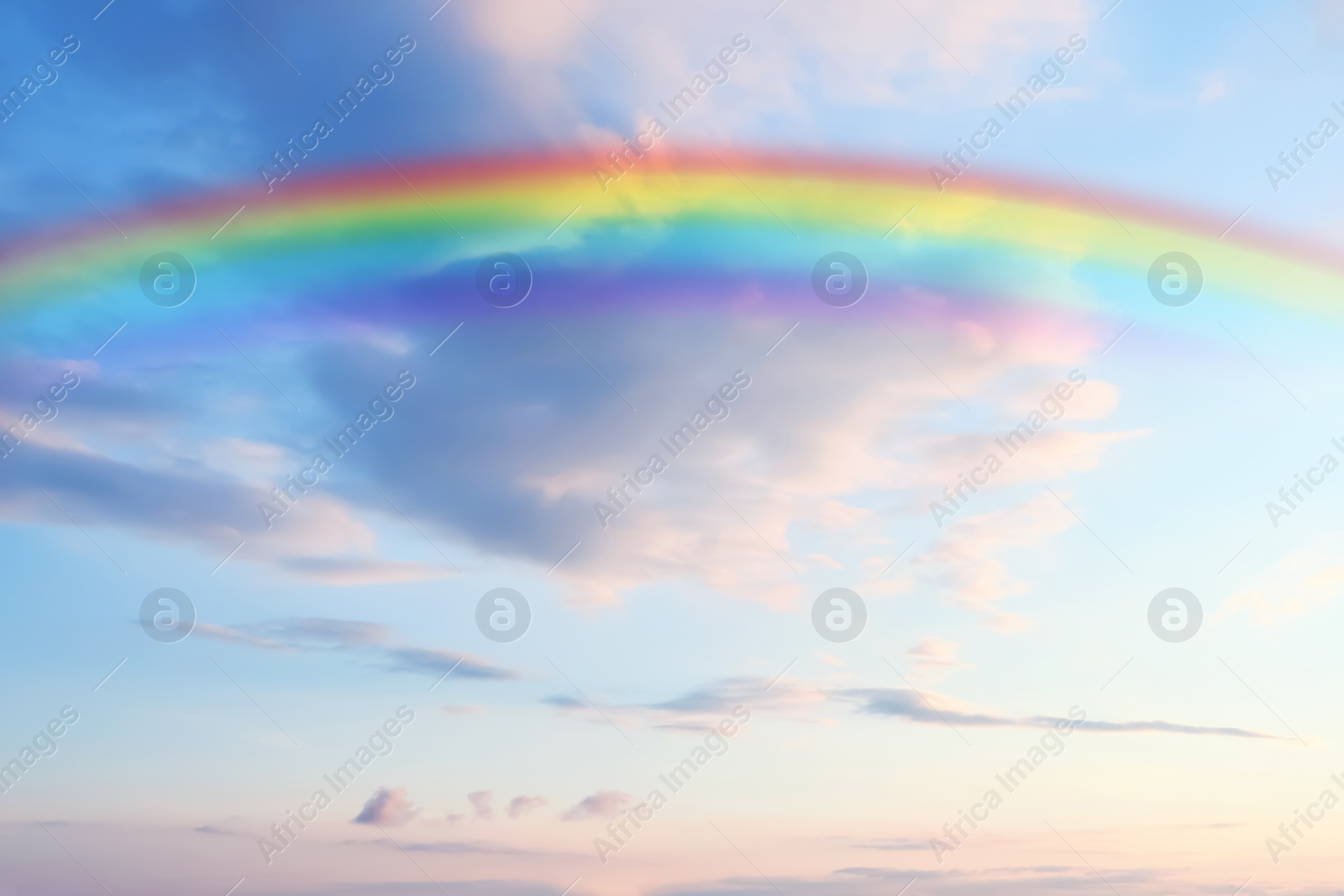 Image of Beautiful rainbow in blue sky with white clouds on sunny day