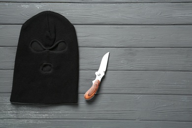 Photo of Black knitted balaclava and knife on grey wooden table, flat lay. Space for text