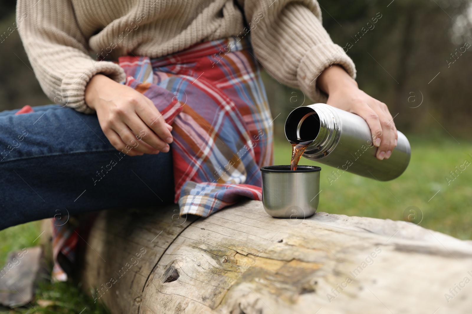 Photo of Woman pouring hot drink from metallic thermos into cup lid outdoors, closeup