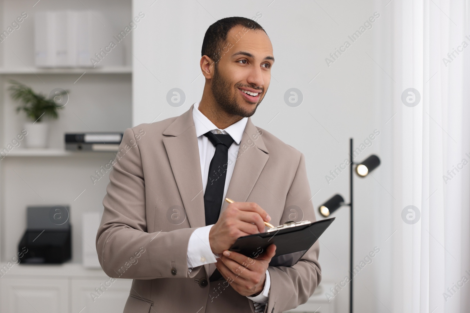 Photo of Smiling young man with clipboard writing notes in office. Lawyer, businessman, accountant or manager