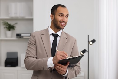 Photo of Smiling young man with clipboard writing notes in office. Lawyer, businessman, accountant or manager