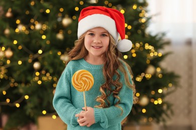 Photo of Happy little girl with lollipop near Christmas tree at home
