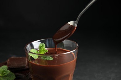 Photo of Taking delicious hot chocolate with spoon on dark background, closeup