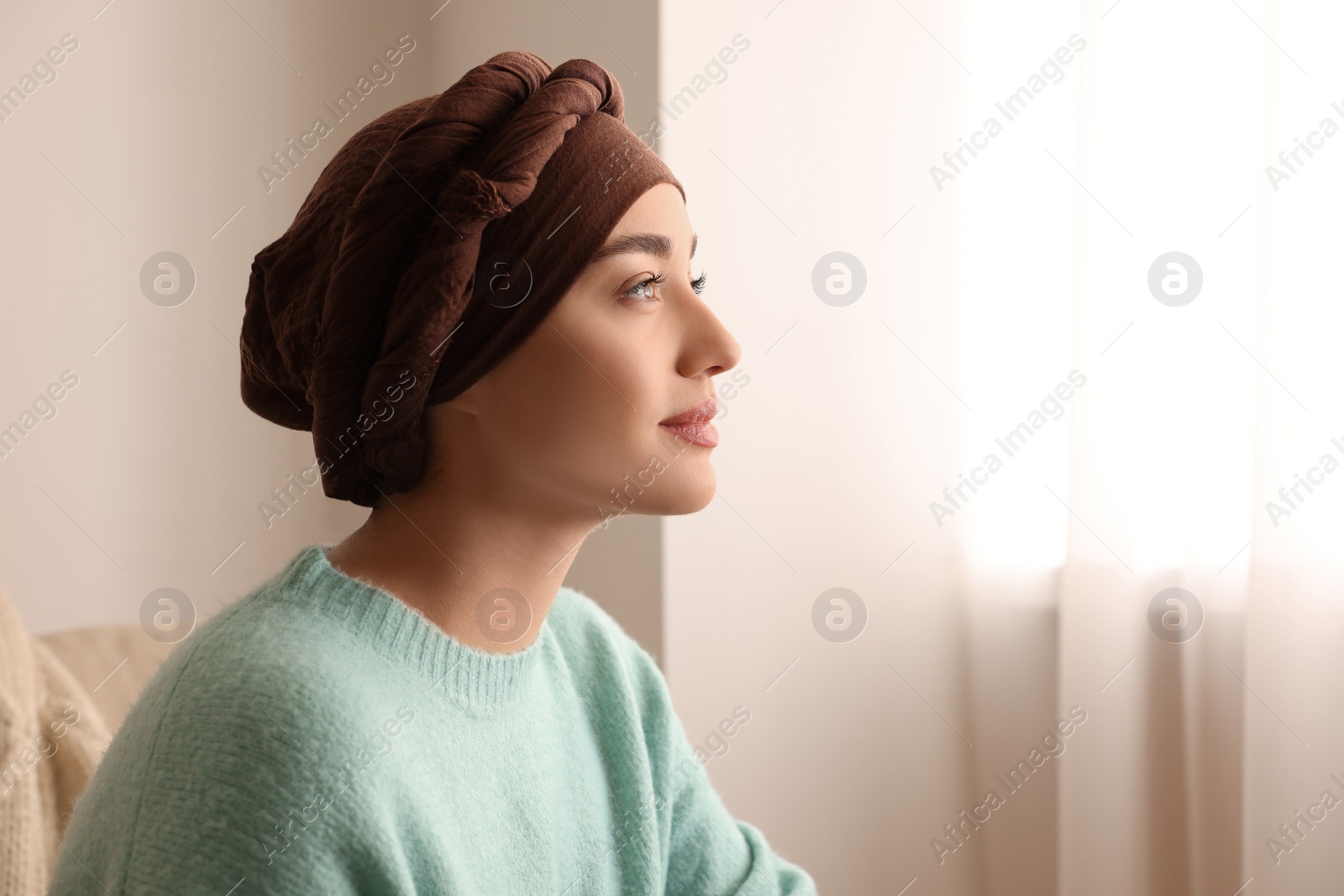 Photo of Cancer patient. Young woman with headscarf near window indoors, space for text