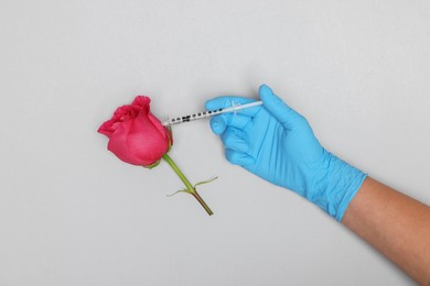 Doctor making injection to rose on light grey background, top view