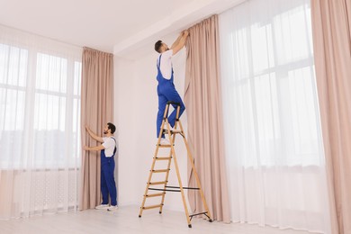 Workers in uniform hanging window curtain indoors