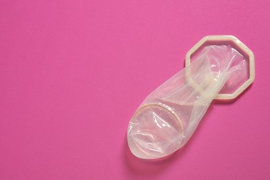 Photo of Unrolled female condom on pink background, top view and space for text. Safe sex