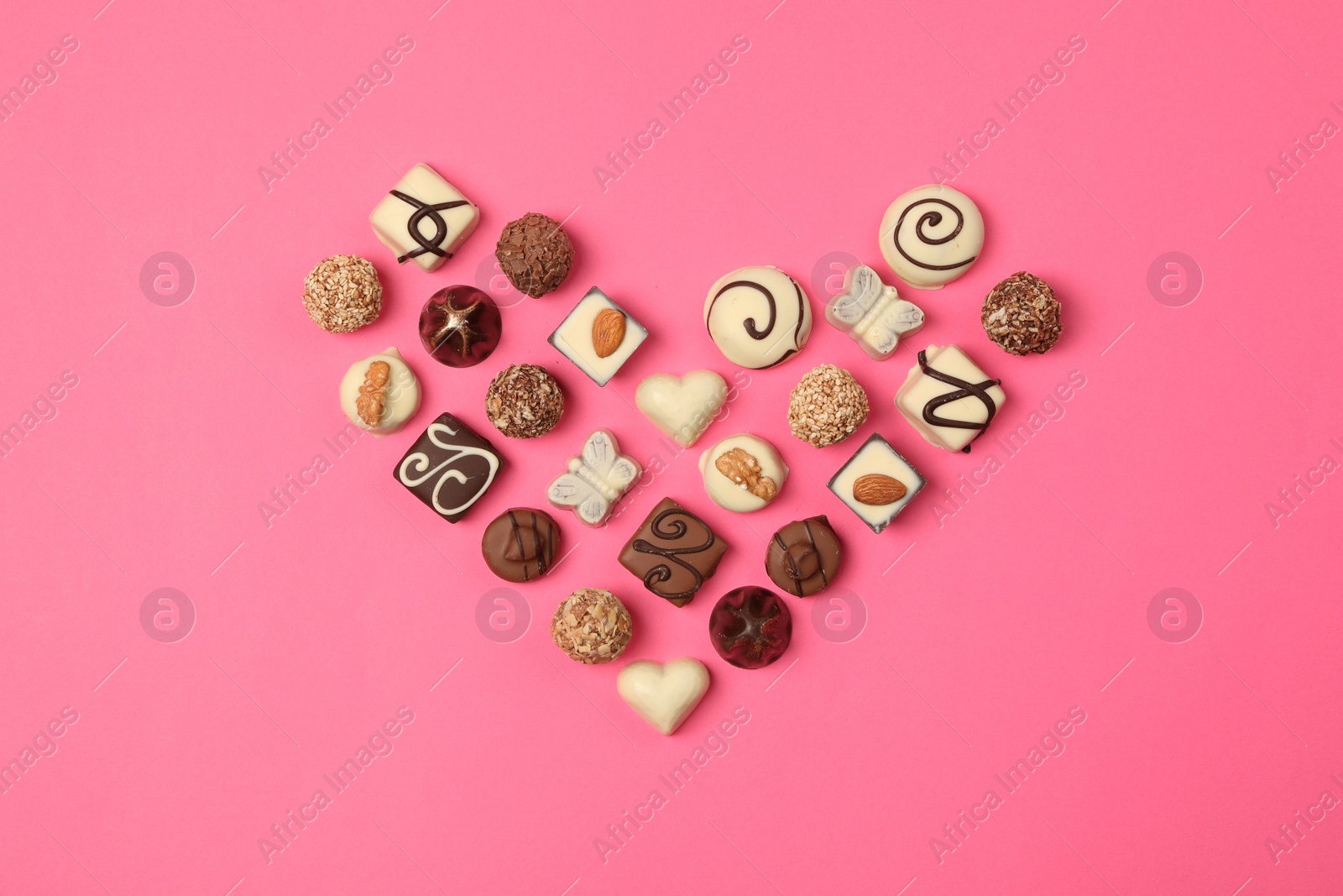 Photo of Heart made with delicious chocolate candies on pink background, top view