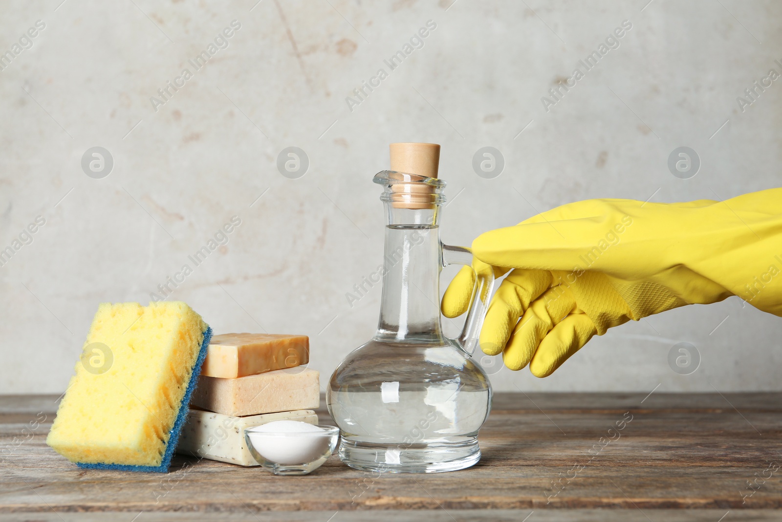 Photo of Woman with jug of vinegar and cleaning supplies at table