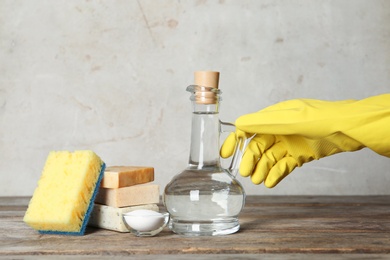 Photo of Woman with jug of vinegar and cleaning supplies at table