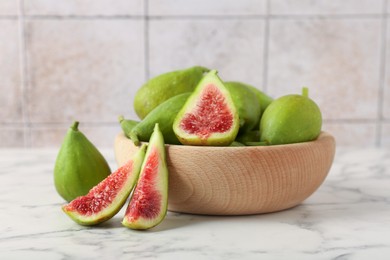 Photo of Cut and whole green figs on white marble table