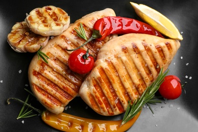 Photo of Tasty grilled chicken fillets with vegetables, lemon slice and rosemary on black plate, flat lay