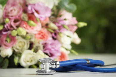 Photo of Stethoscope and flowers on white table against blurred background, space for text. World health day