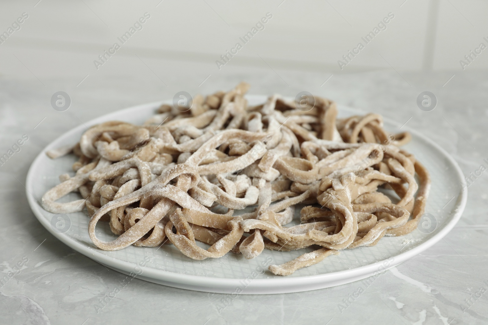 Photo of Uncooked homemade soba (buckwheat noodles) on grey table, closeup